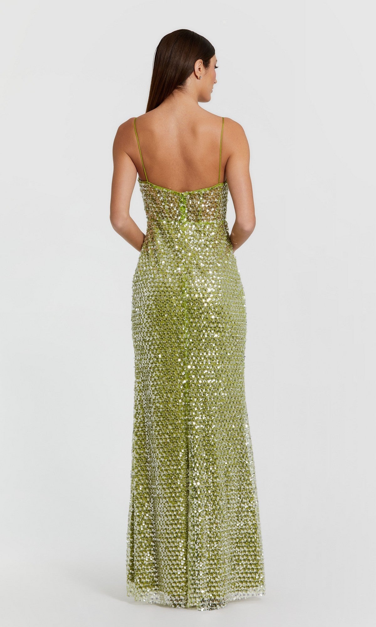 A woman stands facing away against a plain light background, wearing the Mac Duggal 68895 long formal dress—a shimmering green evening gown with sequin embellishments and thin straps.